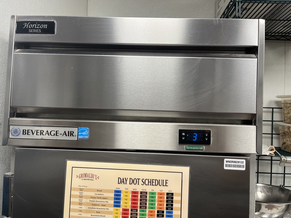 Commercial kitchen refrigeration in a Tampa Bay restaurant — stainless units with day-dot food safety schedule