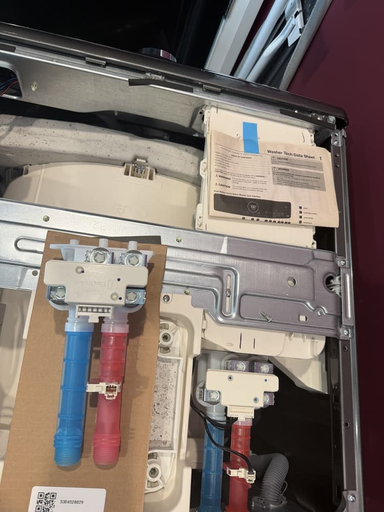 Electrolux front-load washer opened for E11 diagnostics with the old water inlet valve removed and the factory tech data sheet visible