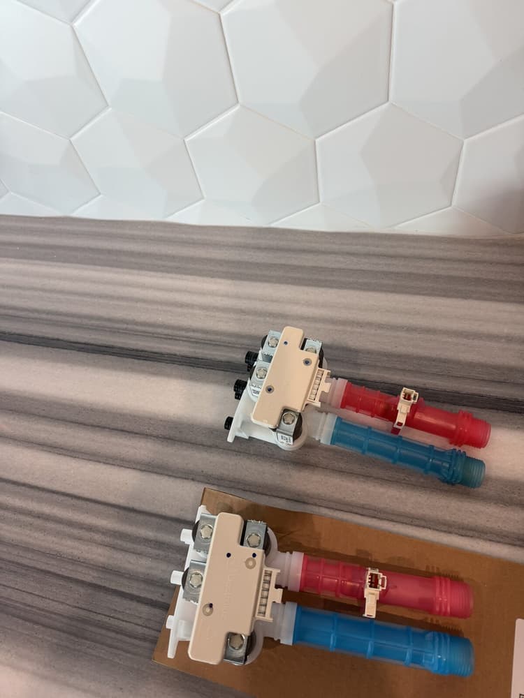 New OEM Electrolux water inlet valve assembly next to the old valve removed during an E11 repair