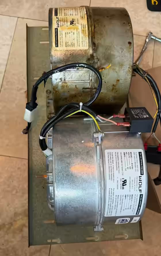 Original grease-coated Wolf 814784 hood blower next to its new replacement on the same mounting plate